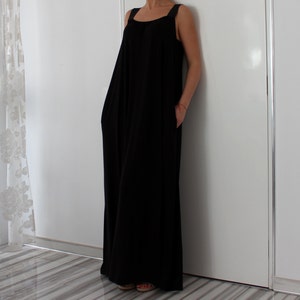 May include: A long black sleeveless maxi dress with a square neckline and thin straps. The dress has a relaxed fit and pockets on the sides.