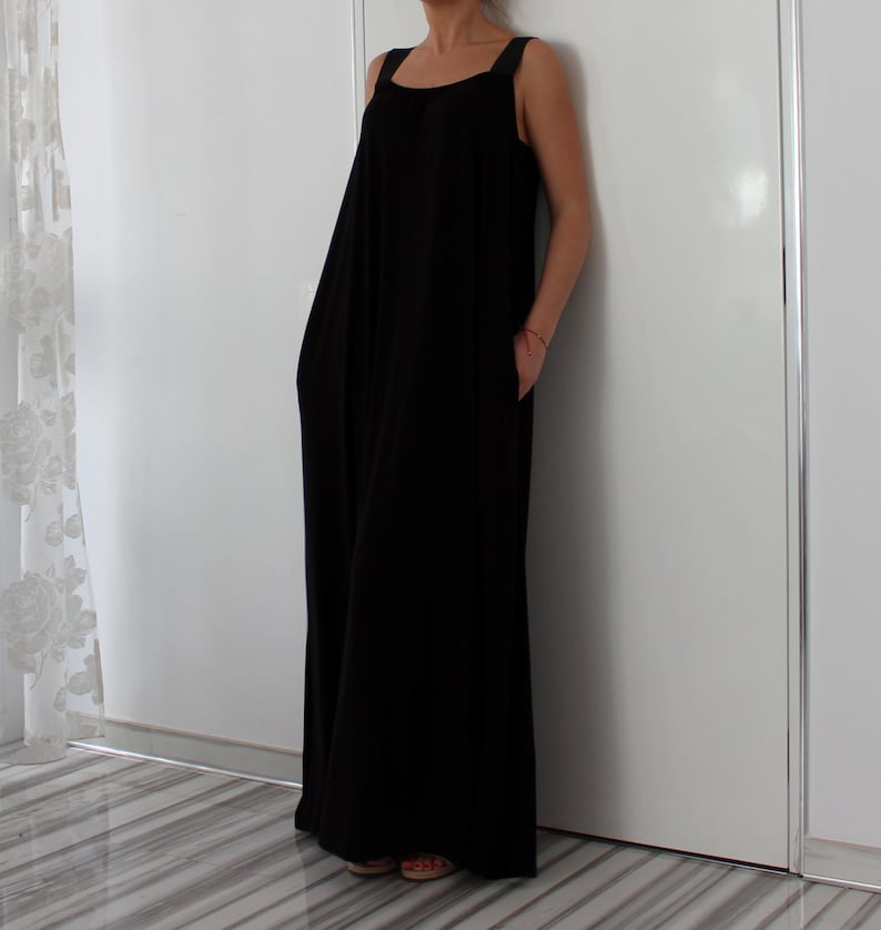 May include: A long black sleeveless maxi dress with a square neckline and thin straps. The dress has a relaxed fit and pockets on the sides.