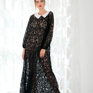 May include: A woman wearing a black lace maxi dress with a white collar and black heels. The dress has a floral pattern and is sheer.