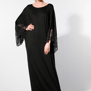 Puede incluir: Vestido negro largo con mangas anchas y pu&ntilde;os de encaje. El vestido tiene un escote redondo y se lleva con sandalias negras. La modelo lleva pendientes de perlas grandes.