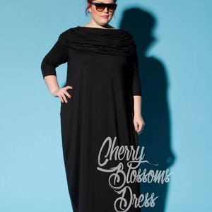 以下が含まれることがあります： ドレープネックと七分袖の黒いマキシ丈ワンピース。 ワンピースには「Cherry Blossoms Dress」の文字が筆記体で入っています。 モデルはサングラスとレオパード柄のヒールを着用し、青い背景に設定されています。