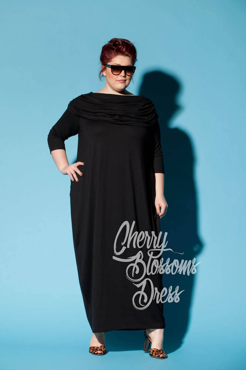 以下が含まれることがあります： ドレープネックと七分袖の黒いマキシ丈ワンピース。 ワンピースには「Cherry Blossoms Dress」の文字が筆記体で入っています。 モデルはサングラスとレオパード柄のヒールを着用し、青い背景に設定されています。