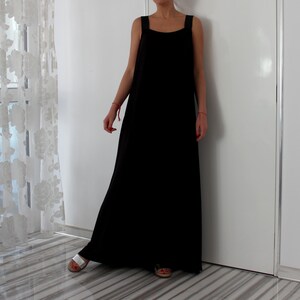 May include: A black sleeveless maxi dress with a square neckline. The dress is made of a soft, flowing fabric and has a relaxed fit.