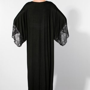 Puede incluir: Un vestido largo negro con mangas anchas y detalles de encaje en los pu&ntilde;os. El vestido tiene un dise&ntilde;o simple y elegante y una silueta fluida. La modelo est&aacute; de espaldas a la c&aacute;mara, mostrando la parte trasera del vestido.