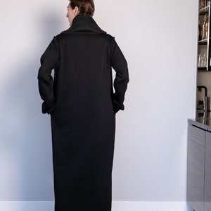 May include: A long black coat with a high collar and a relaxed fit. The coat is made of a soft, comfortable fabric and has a simple, elegant design.