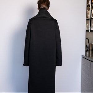 May include: A long black coat with a high collar and long sleeves. The coat is made of a soft, comfortable fabric and has a relaxed fit.