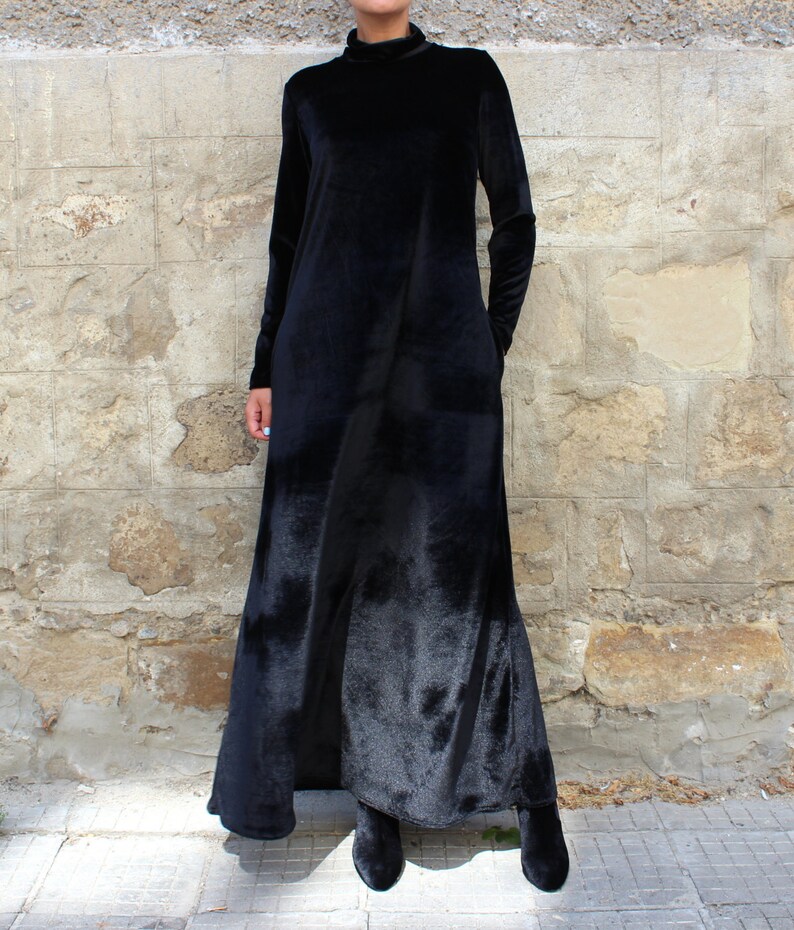 May include: A long black velvet dress with a mock neck and long sleeves. The dress has a flowing silhouette and is made of a soft, luxurious fabric.