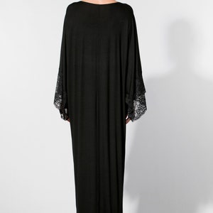 Puede incluir: Vestido largo negro con mangas anchas y pu&ntilde;os de encaje. El vestido tiene un dise&ntilde;o sencillo y elegante. La persona lleva el pelo recogido y pendientes grandes. Adecuado para eventos nocturnos.