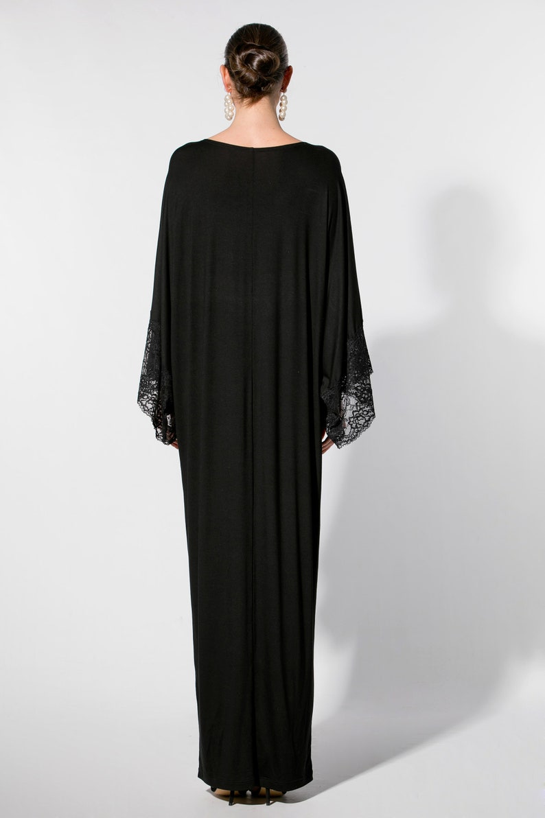 Puede incluir: Vestido largo negro con mangas anchas y pu&ntilde;os de encaje. El vestido tiene un dise&ntilde;o sencillo y elegante. La persona lleva el pelo recogido y pendientes grandes. Adecuado para eventos nocturnos.
