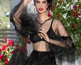 Puede incluir: Una mujer con un top negro transparente con un dobladillo con volantes y un sujetador negro debajo. También lleva una falda negra de cintura alta con un dobladillo con volantes. Tiene el pelo oscuro y lleva pendientes de aro dorados.