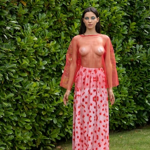May include: A woman wearing a red sheer top and a pink skirt with a cherry print. She is wearing pink platform sandals.