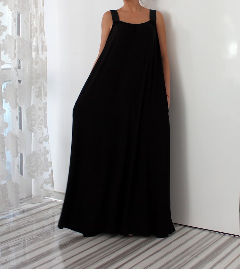 May include: A black sleeveless maxi dress with a simple, loose fit. The dress has thin straps and a scoop neckline.