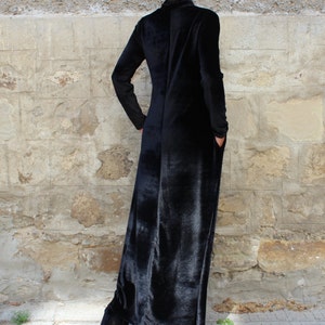May include: A long black velvet dress with a mock neck and long sleeves. The dress has a straight silhouette and falls to the ankles.