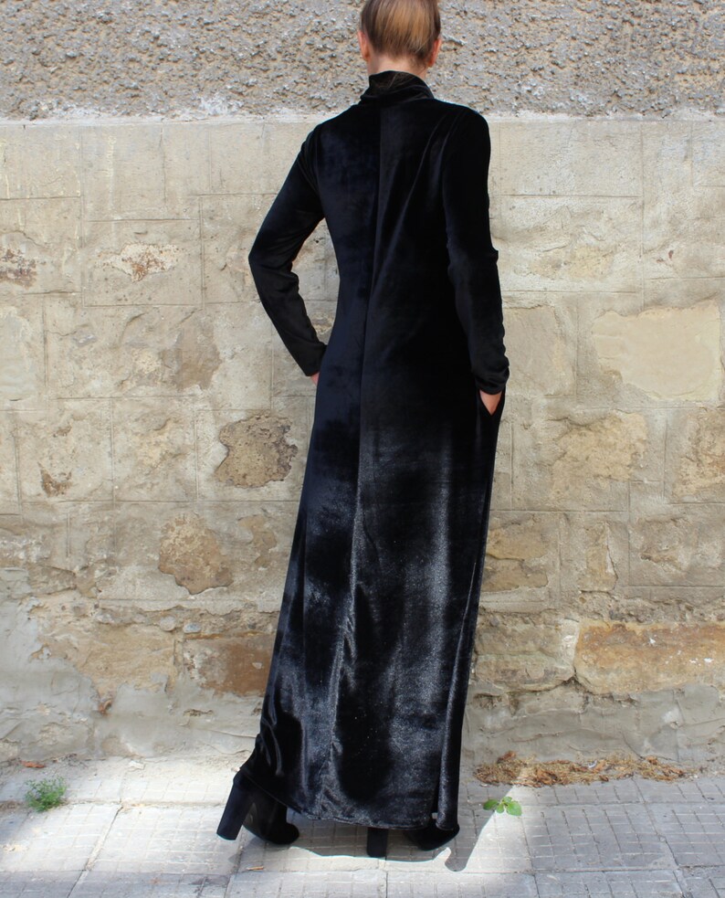 May include: A long black velvet dress with a mock neck and long sleeves. The dress has a straight silhouette and falls to the ankles.