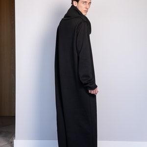 May include: A long black hooded sweater with a high collar and a relaxed fit. The sweater is made of a soft, comfortable fabric and has a slightly distressed hem.