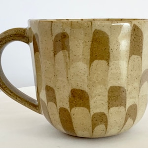 May include: A ceramic mug with a brown and beige geometric pattern. The mug has a rounded shape and a handle.