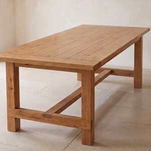 May include: A rectangular dining table constructed from light brown wood with a visible grain pattern. The tabletop consists of several parallel planks, supported by four sturdy square legs connected by a horizontal stretcher bar near the base.