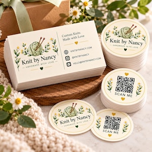 Könnte beinhalten: Ein Stapel rechteckiger Visitenkarten und mehrere Stapel runder Aufkleber mit einem grünen Wollknäuel, Stricknadeln, Blumenmotiven und dem Text Knit by Nancy. Einige Aufkleber zeigen einen QR-Code mit der Aufschrift SCAN ME.
