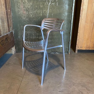 May include: An aluminum and wood chair with a slatted back and seat. The chair has a silver frame and armrests with wooden accents. The chair is a vintage design, suitable for indoor or outdoor use.