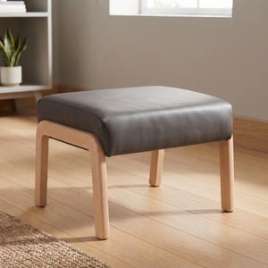 May include: A square ottoman featuring a smooth, dark charcoal gray upholstered seat cushion supported by four light-toned natural wood legs with rounded corners, providing a stable base for this piece of furniture.