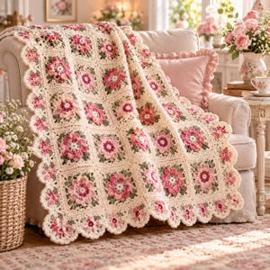 May include: A handmade crochet blanket featuring a repeating square pattern with cream-colored borders and central floral motifs in shades of pink, magenta, and sage green. The blanket has a scalloped edge and a textured, yarn-based construction.
