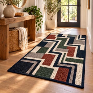 Könnte beinhalten: Ein rechteckiger Teppich mit einem geometrischen Muster aus ineinandergreifenden Linien und Blöcken in Marineblau, Creme, Waldgrün, Terrakotta und Grau. Der Teppich hat eine strukturierte, gewebte Oberfläche und liegt auf einem hellen Holzboden.