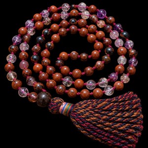 Könnte beinhalten: Eine Mala-Kette mit abwechselnden runden Mahagoni-Obsidian-Perlen und klaren Quarzperlen mit violetten Einschlüssen. Die Perlen sind auf eine dunkelrosa Schnur gefädelt und enden in einer großen dunklen Perle sowie einer dicken, mehrfarbigen Quaste.