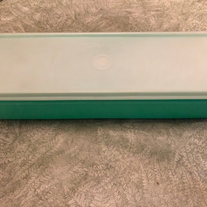 May include: A light green rectangular plastic container with a white lid. The lid has a small circle in the center.