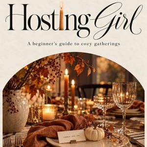 Può includere: Una copertina di libro intitolata The Fall Hosting Girl: A beginner's guide to cozy gatherings. L'immagine mostra una tavola apparecchiata con piatti bianchi, un tovagliolo color ruggine, una piccola zucca bianca, un segnaposto e candele.