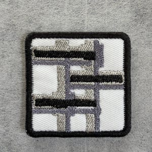 May include: A square embroidered patch featuring a white background with a black border. The design consists of overlapping horizontal and vertical bars in shades of grey and black, creating a geometric grid pattern with a textured thread finish.