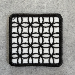 May include: A square embroidered patch featuring a repeating geometric pattern of black interlocking circles and ovals on a white background, finished with a thick black stitched border around the entire perimeter of the square shape.