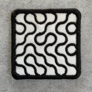 May include: A square-shaped embroidered patch featuring a white background with a black border and a continuous, winding black line pattern that creates organic, maze-like shapes across the entire surface of the fabric accessory.