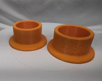 May include: Two orange cylindrical objects with a textured surface and a wide circular base. Each object features a hollow center and a smooth, flat rim at the top. The items are positioned side by side, with one being noticeably larger in diameter.