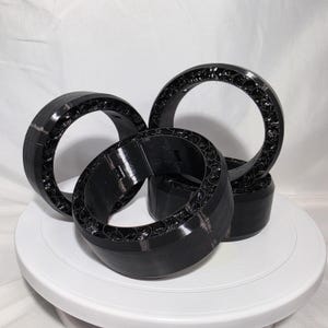 May include: Three black circular rings with a smooth outer surface and a complex, web-like internal structure. The rings are arranged in a cluster, showcasing the contrast between the solid exterior walls and the intricate, porous inner design.