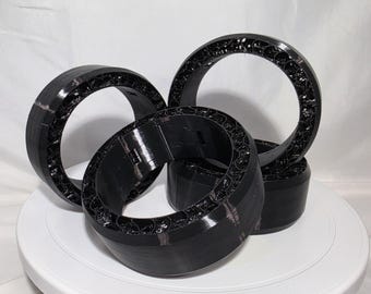 May include: Three black circular rings with a smooth outer surface and a complex, web-like internal structure. The rings are arranged in a cluster, showcasing the contrast between the solid exterior walls and the intricate, porous inner design.