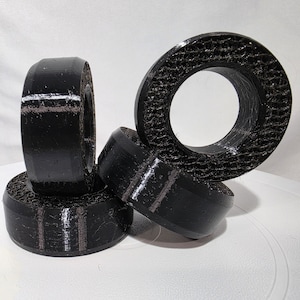 May include: Three black, circular, 3D-printed objects with a smooth outer rim and a textured, honeycomb-like interior structure. The items are arranged in a cluster, with one standing vertically and two positioned horizontally at the base.
