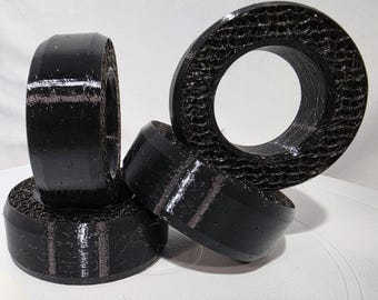 May include: Three black, circular, 3D-printed objects with a smooth outer rim and a textured, honeycomb-like interior structure. The items are arranged in a cluster, with one standing vertically and two positioned horizontally at the base.