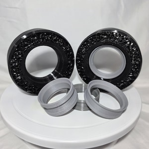 May include: Two large black circular rings with a textured, porous outer surface and smooth grey inner rims, accompanied by three smaller, smooth grey circular rings of varying sizes, all arranged together in a cluster.