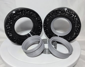 May include: Two large black circular rings with a textured, porous outer surface and smooth grey inner rims, accompanied by three smaller, smooth grey circular rings of varying sizes, all arranged together in a cluster.