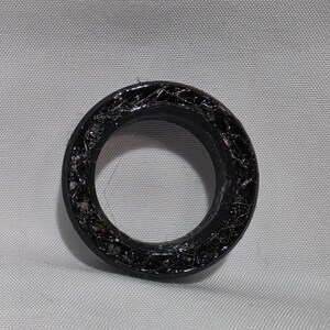 May include: A circular black ring featuring a textured, web-like interior surface with a glossy finish. The object has a smooth outer rim and a hollow center, displaying a dark, intricate pattern throughout the inner band structure.
