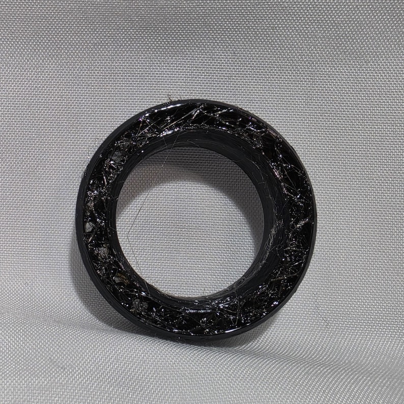 May include: A circular black ring featuring a textured, web-like interior surface with a glossy finish. The object has a smooth outer rim and a hollow center, displaying a dark, intricate pattern throughout the inner band structure.