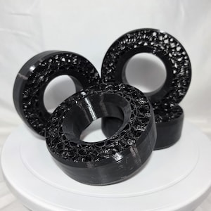 May include: Three black circular components with a hollow center and a porous, honeycomb-like internal structure. The outer edges are smooth and solid, while the interior surfaces feature a complex, webbed pattern of interconnected black material.