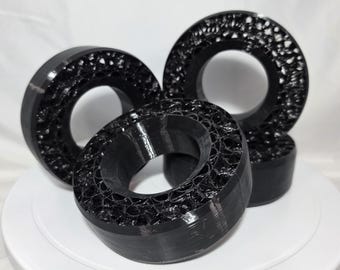 May include: Three black circular components with a hollow center and a porous, honeycomb-like internal structure. The outer edges are smooth and solid, while the interior surfaces feature a complex, webbed pattern of interconnected black material.