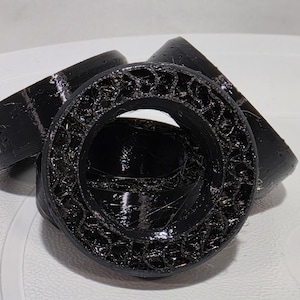 May include: Three black circular components with a hollow center and a textured, lattice-like interior structure. The outer edges are smooth and glossy, while the inner ring features a complex, repeating geometric pattern.