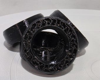 May include: Three black circular components with a hollow center and a textured, lattice-like interior structure. The outer edges are smooth and glossy, while the inner ring features a complex, repeating geometric pattern.