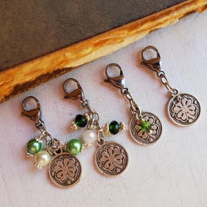 May include: Four silver charm pendants with four-leaf clover designs. Each pendant has a silver lobster clasp and is adorned with green and white beads.