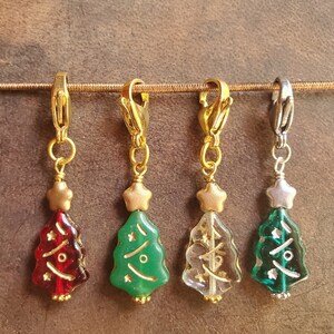 May include: Four Christmas tree-shaped glass charms with gold and silver accents. The charms are red, green, clear, and green. Each charm has a gold star on top and a gold or silver clip.
