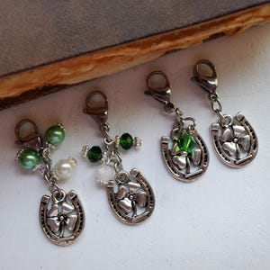 May include: Four silver charm clips with a horseshoe and four-leaf clover design. Each charm has green and white beads and a green crystal.