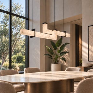 May include: A linear pendant light fixture featuring three interconnected rectangular bars made of translucent white stone with visible veining. The bars are held together by black metal brackets and suspended from the ceiling by thin black wires.