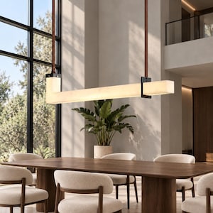 May include: A linear pendant light fixture featuring a long, rectangular, translucent white bar suspended by two brown leather straps attached to black metal brackets. The light emits a soft, even glow across its horizontal length.
